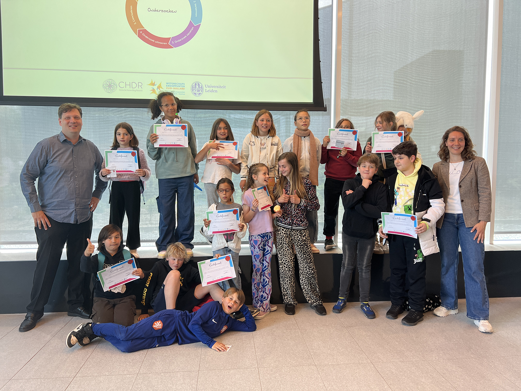 Een man en een vrouw poseren met een groep kinderen die blij hun certificaten laten zien.
