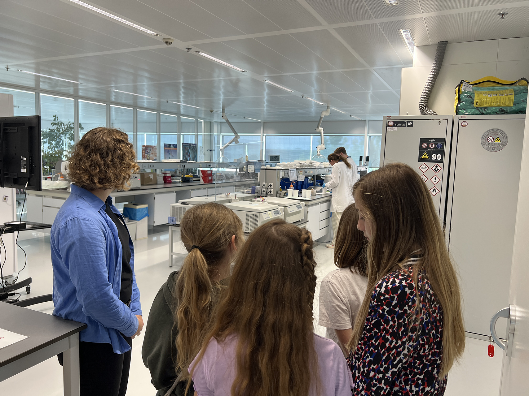 Kinderen krijgen uitleg over een laboratoriumruimte, met laboratoriumapparatuur op de achtergrond.