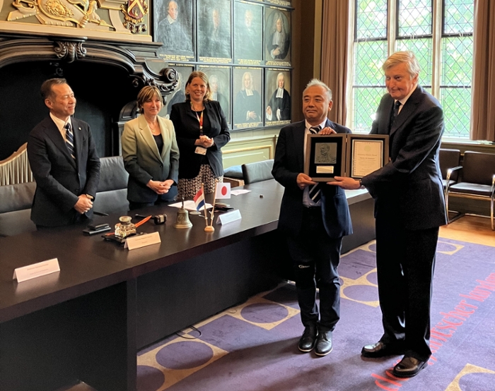 Drie bestuursleden van de Universiteit Leiden en Nagasaki University kijken hoe Pancras Hoogendoorn samen met Ikematsu Kazuya poseert met de award die hij net heeft gekregen.