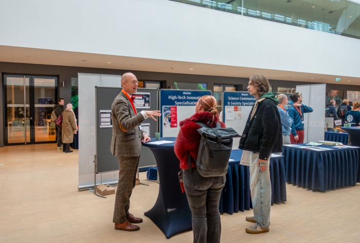 Een man in pak die aan een tafel staat geeft een vrouwelijke en mannelijke student uitleg.