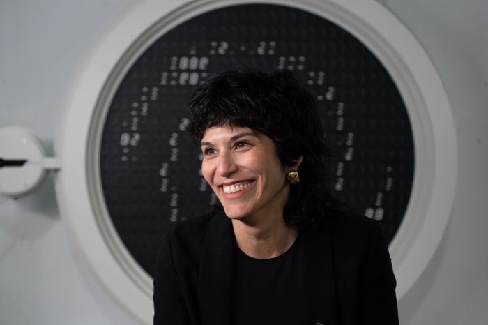 Yamila Miguel voor het ronde kunstwerk. Binnen een witte rand is een zwart vlak te zien waar flipdots kunnen omdraaien.
