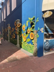 Straathoek in Willemstad, Curaçao, met een blauwe muur met geschilderde zonnebloemen.