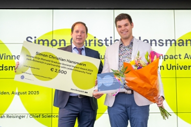 Hans Roubos (links) met reikt een chêque en een bos bloemen uit aan Simon Christian Hansmann.