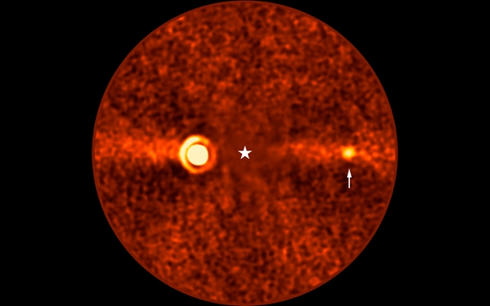 De ontdekte planeet Beta Pictoris d (bij de witte pijl) op een opname van de Very Large Telescope. Het licht van de ster Beta Pictoris is geblokkeerd (op de plek van de witte ster). Links is de veel grotere planeet Beta Pictoris b zichtbaar. (c) ESO/B. Sutlieff, M. Bonse et al.