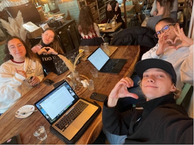 Groep van vier antropologiestudenten met hun laptop in een café maken hartgebaren met hun handen.
